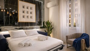 A modern hotel room with a bed, a chair, a potted plant, and a framed picture on the wall.