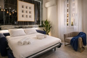 A modern hotel room with a bed, a seating area, and a large window.