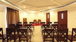 A conference room with rows of wooden chairs, a red carpet, and a ceiling fan. - HOTEL DIAMOND FORT (Karunagappally)