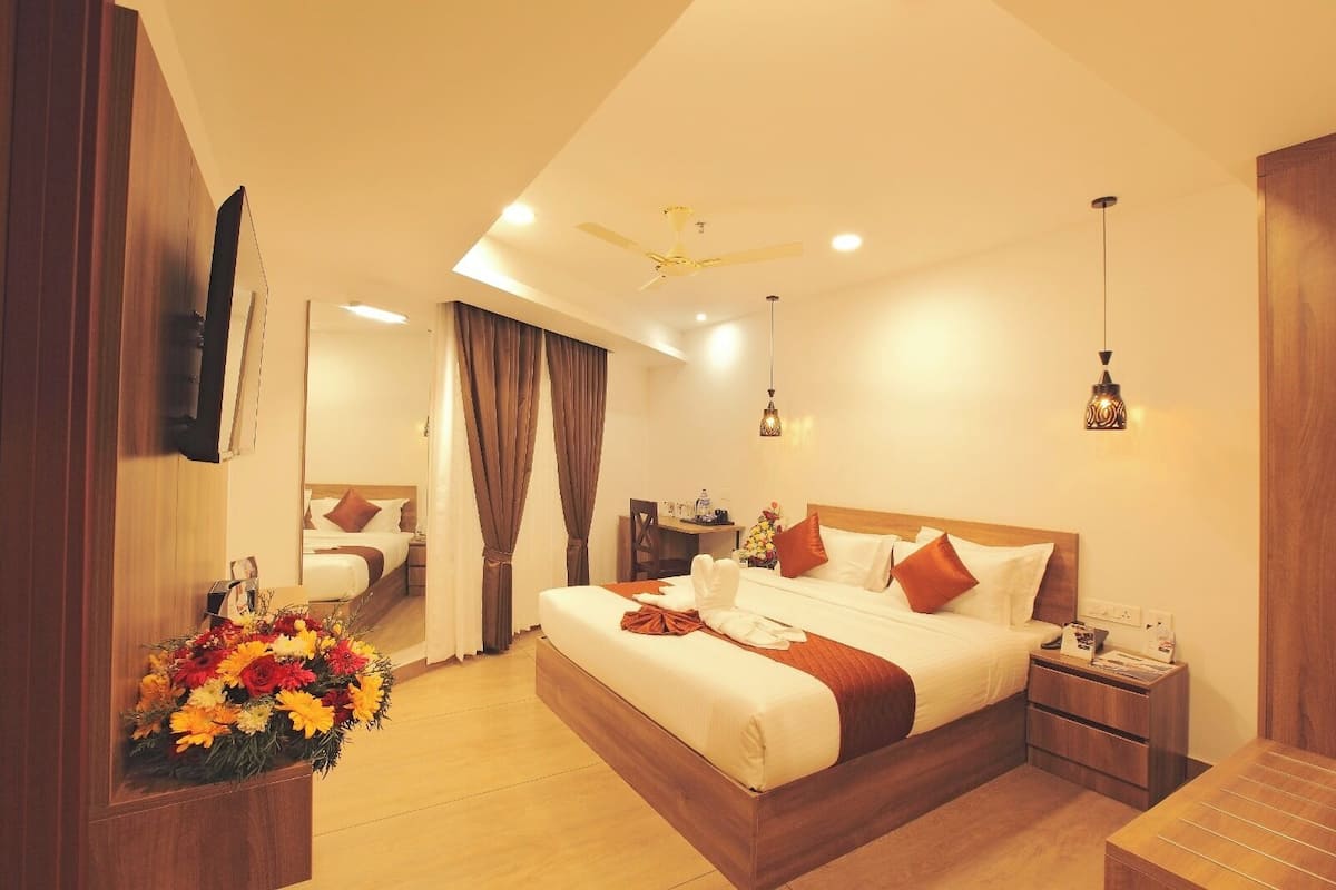 A hotel room with a large bed, a desk, a chair, a mirror, and a flower arrangement.
