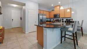 A modern kitchen with a central island, wooden cabinets, stainless steel appliances, and pendant lighting. - Family House near Disney - 5109 (Kissimmee)