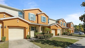 A row of two-story houses with attached garages, a well-maintained lawn, and a clear sky. - Family House near Disney - 5109 (Kissimmee)