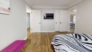 A bedroom with a bed, a bench, a TV, and a wardrobe. - Grosse Pointe Retreat | 3BR, Sleeps 8 & Relaxing (Grosse Pointe)