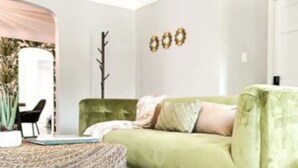 A room with a green sofa, a woven coffee table, a plant, and a door with a mirror. - Grosse Pointe Retreat | 3BR, Sleeps 8 & Relaxing (Grosse Pointe)