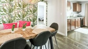 A dining area with a wooden table, black chairs, a hanging light fixture, and a wall with a leafy pattern. - Grosse Pointe Retreat | 3BR, Sleeps 8 & Relaxing (Grosse Pointe)