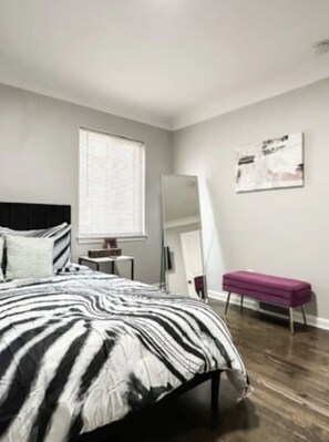 A bedroom with a bed, a bench, a mirror, and a window.
