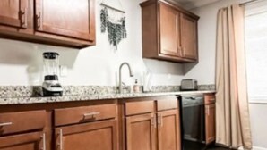 A kitchen with wooden cabinets, a granite countertop, a coffee maker, and a dishwasher. - Grosse Pointe Retreat | 3BR, Sleeps 8 & Relaxing (Grosse Pointe)