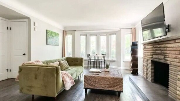 A living room with a green sofa, a coffee table, a fireplace, and a TV mounted on the wall. - Grosse Pointe Retreat | 3BR, Sleeps 8 & Relaxing (Grosse Pointe)