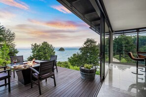 Enjoy ocean views and al fresco dining on this spacious deck with a table for two, surrounded by lush greenery and glass doors.