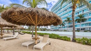 A beachside hotel with thatched umbrellas, lounge chairs, and a pool. - Marítima Beach Condo, 2BR, Deluxe, 2 Pools, BBQ, Balconies & Great Amenities (Flamingos)
