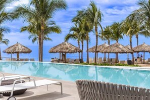 Un espace aménagé au bord de la piscine, avec des chaises longues, des parasols en chaume et des palmiers.
