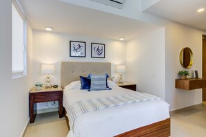 Un dormitorio con una cama grande, dos mesitas de noche, un espejo en la pared y dos obras de arte enmarcadas.