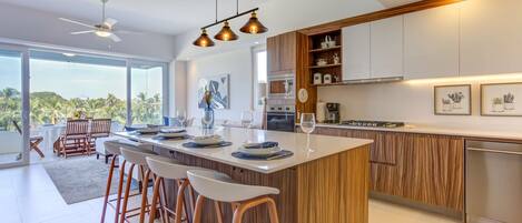 A modern kitchen with a central island, bar stools, and a dining area with a view.