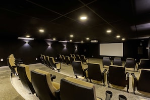 Un teatro con hileras de asientos, una pantalla grande y luces en el techo.