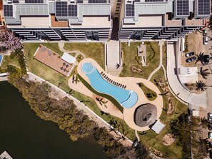 Vista aérea de un moderno complejo residencial con piscina, jardines ajardinados y paneles solares en los tejados.