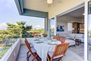 Un coin repas avec une table dressée pour quatre personnes, un canapé et un balcon offrant une vue sur la verdure.