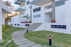 Un edificio moderno con una escalera central, plantas en macetas y un césped bien cuidado.