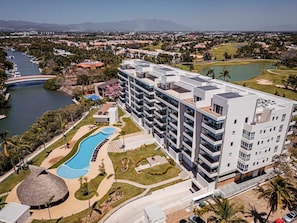 Un hôtel moderne à plusieurs étages, doté d’une piscine et offrant une vue sur une rivière et des montagnes en arrière-plan.
