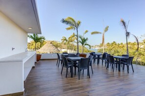 An outdoor dining area with multiple tables and chairs, a thatched-roof structure, and a view of palm trees and a body of water. - Casa Azul New Deluxe Studio Apt w/Great Views, Pool & Jacuzzi (Nuevo Nayarit)