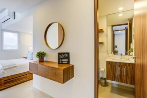 Un dormitorio moderno con cama de madera, una mesita de noche con una planta y un letrero, un espejo grande y vistas al baño.