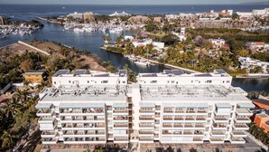 A modern hotel with multiple floors, rooftop solar panels, and a marina in the background.