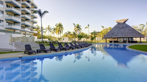 A swimming pool with lounge chairs and a thatched-roof structure.