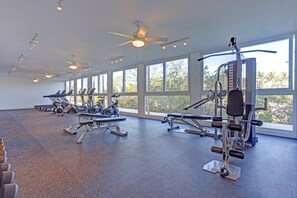 Un gimnasio con diverso equipo de ejercicio, ventanas amplias y ventiladores de techo.