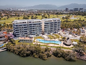 A modern hotel with multiple floors, a swimming pool, and a golf course in the background. - Casa Azul New Deluxe Studio Apt w/Great Views, Pool & Jacuzzi (Nuevo Nayarit)