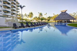 Una piscina con sillas de descanso y una estructura de techo de paja.