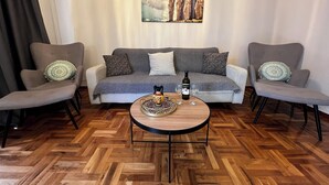 Ein Wohnzimmer mit einem grauen Sofa, zwei Sesseln, einem Couchtisch mit einer Flasche und Gläsern sowie einem Gemälde über dem Sofa.