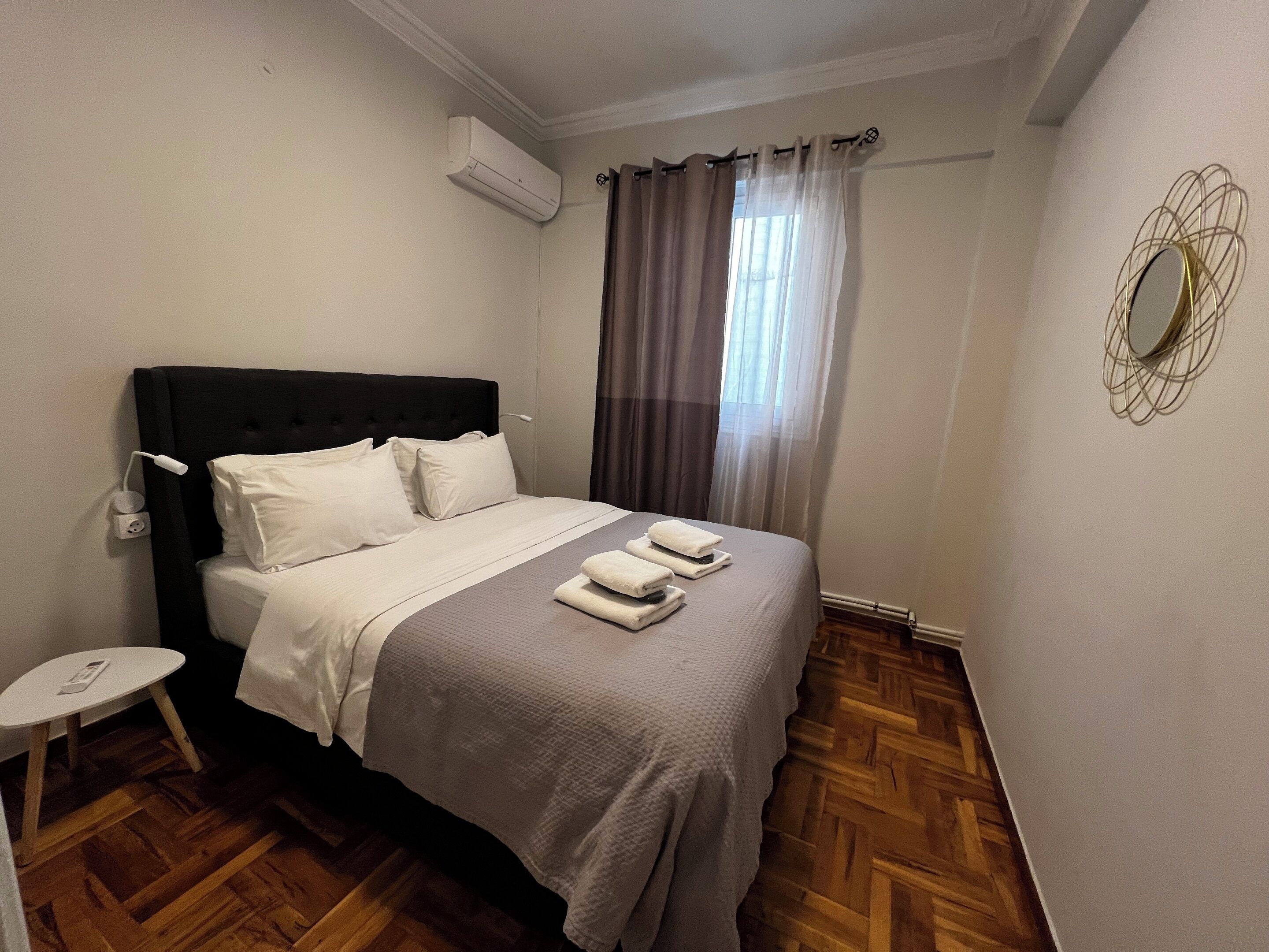 A neatly made bed with white linens, a bedside table with a lamp, and a window with curtains.