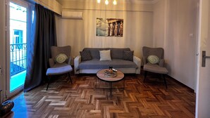 Ein Wohnzimmer mit Fischgrätparkett, einer grauen Sofagarnitur, zwei Sesseln, einem Couchtisch und einer Deckenleuchte.