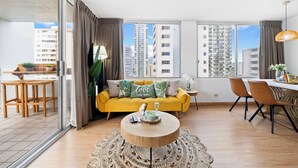 A modern living room with a yellow sofa, a round coffee table, and a dining area with chairs and a table. - NEW! Sweet&Cozy 9thFl  1-BR king Bed (Honolulu)