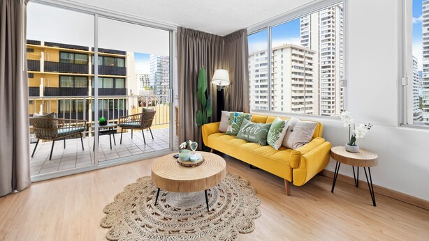 A modern living room with a yellow sofa, a round wooden coffee table, and a view of tall buildings through large windows. - NEW! Sweet&Cozy 9thFl  1-BR king Bed (Honolulu)