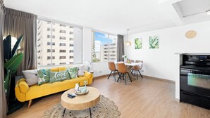 A modern living room with a yellow sofa, dining table, and a kitchen area with an oven. - NEW! Sweet&Cozy 9thFl  1-BR king Bed (Honolulu)