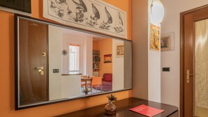 Une pièce avec un grand miroir, une commode en bois, une petite plante et une carte rouge posée sur la commode.