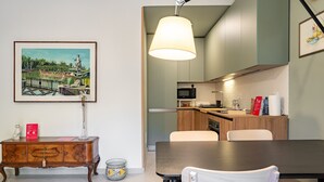 A dining area with a table and chairs, a cabinet with decorative items, and a kitchen in the background. - Casa Gianna by Wonderful Italy (Siracusa)