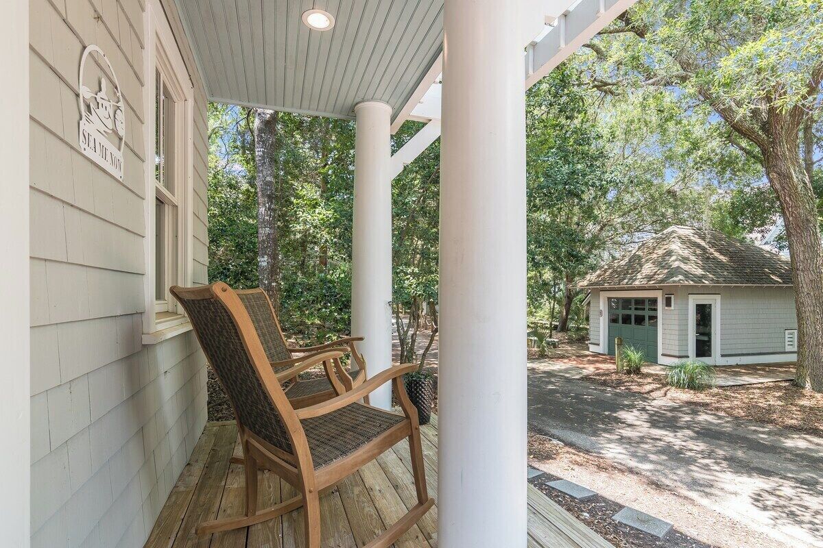 A porch with wooden rocking chairs, a covered area with white columns, and a small building with a green door in the background.