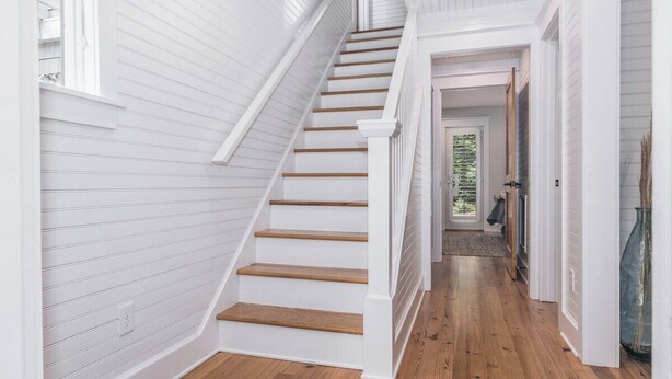Un escalier aux murs blancs et aux marches en bois menant à une porte.