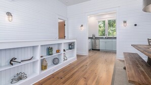 Un intérieur spacieux avec un lambris blanc, un banc en bois et un coin cuisine doté d’une fenêtre.