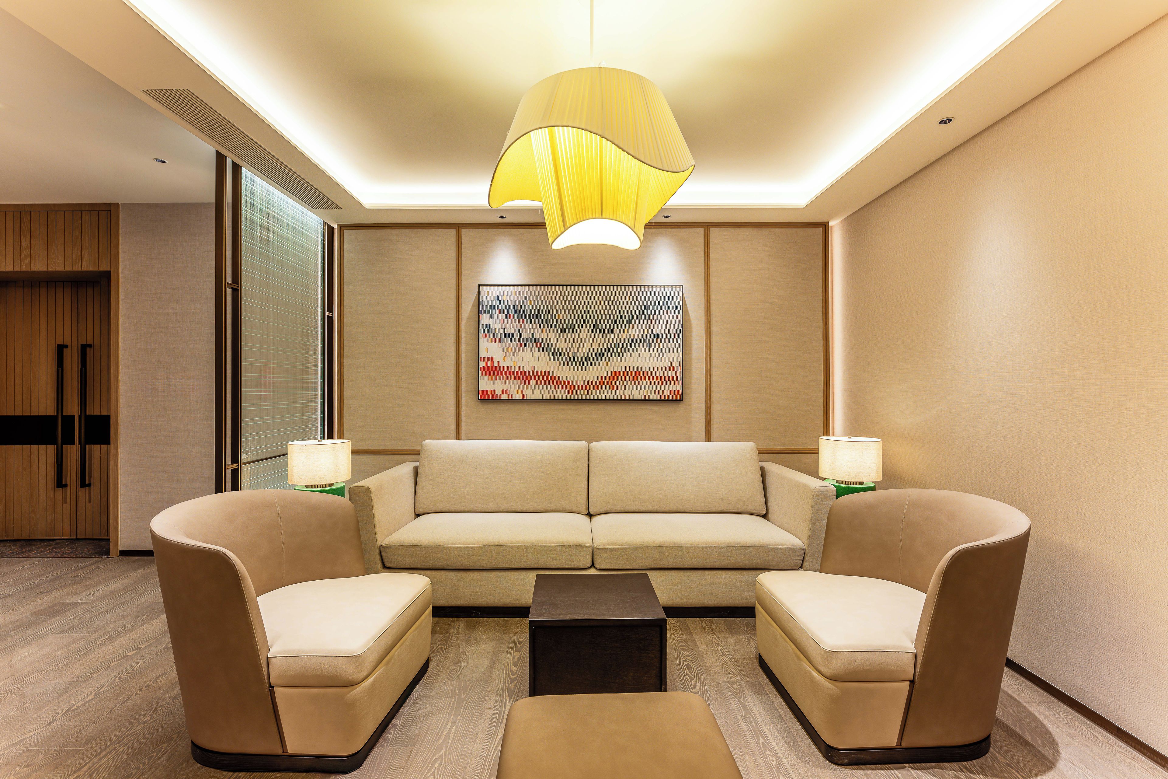 Un salon moderne comprenant un canapé, deux fauteuils, une table basse et un grand tableau abstrait accroché au mur.