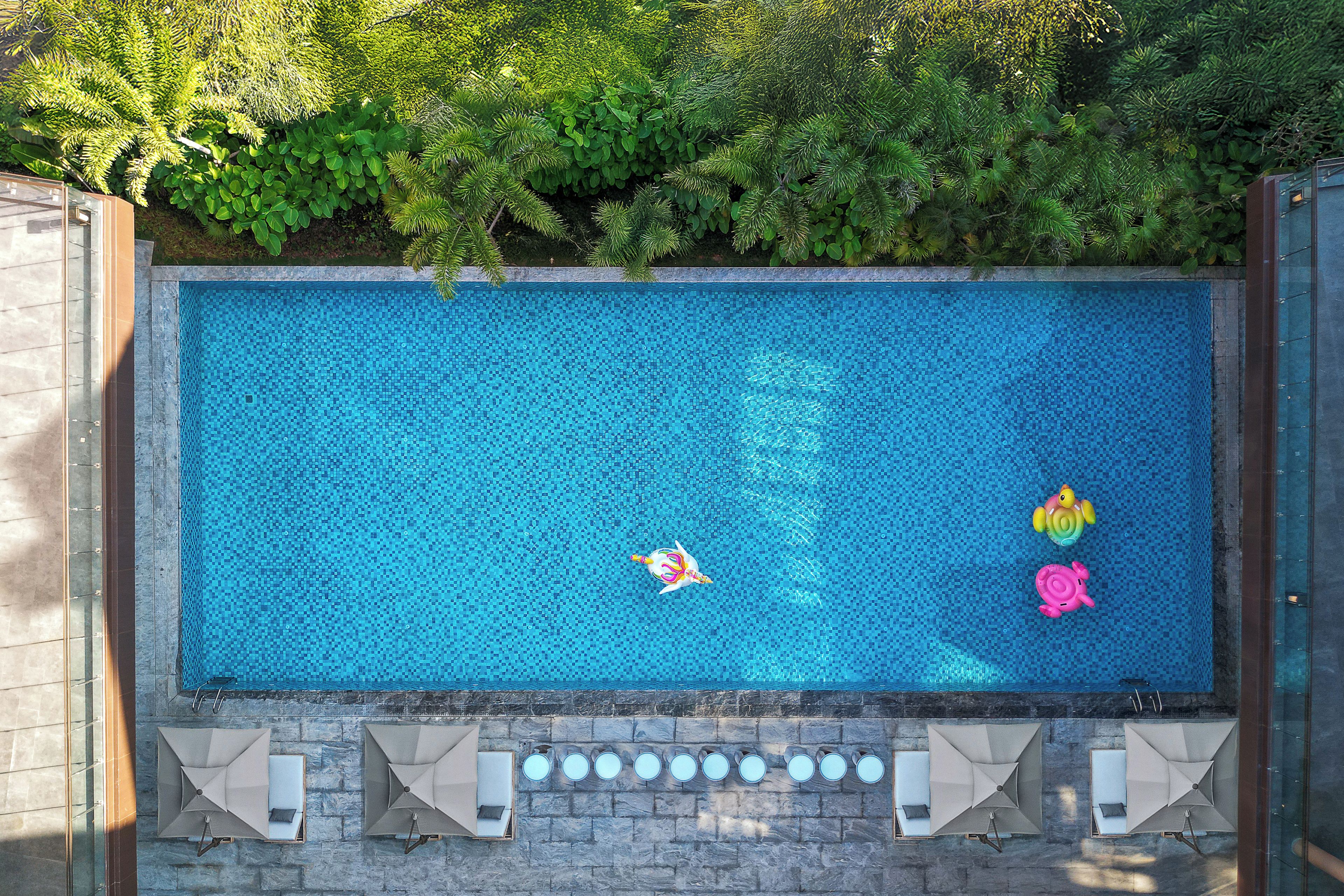 Piscina rectangular con superficie de azulejos, rodeada por una pared de piedra y una terraza de madera.