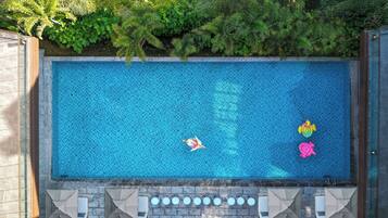 Piscina rectangular con superficie de azulejos, rodeada por una pared de piedra y una terraza de madera.