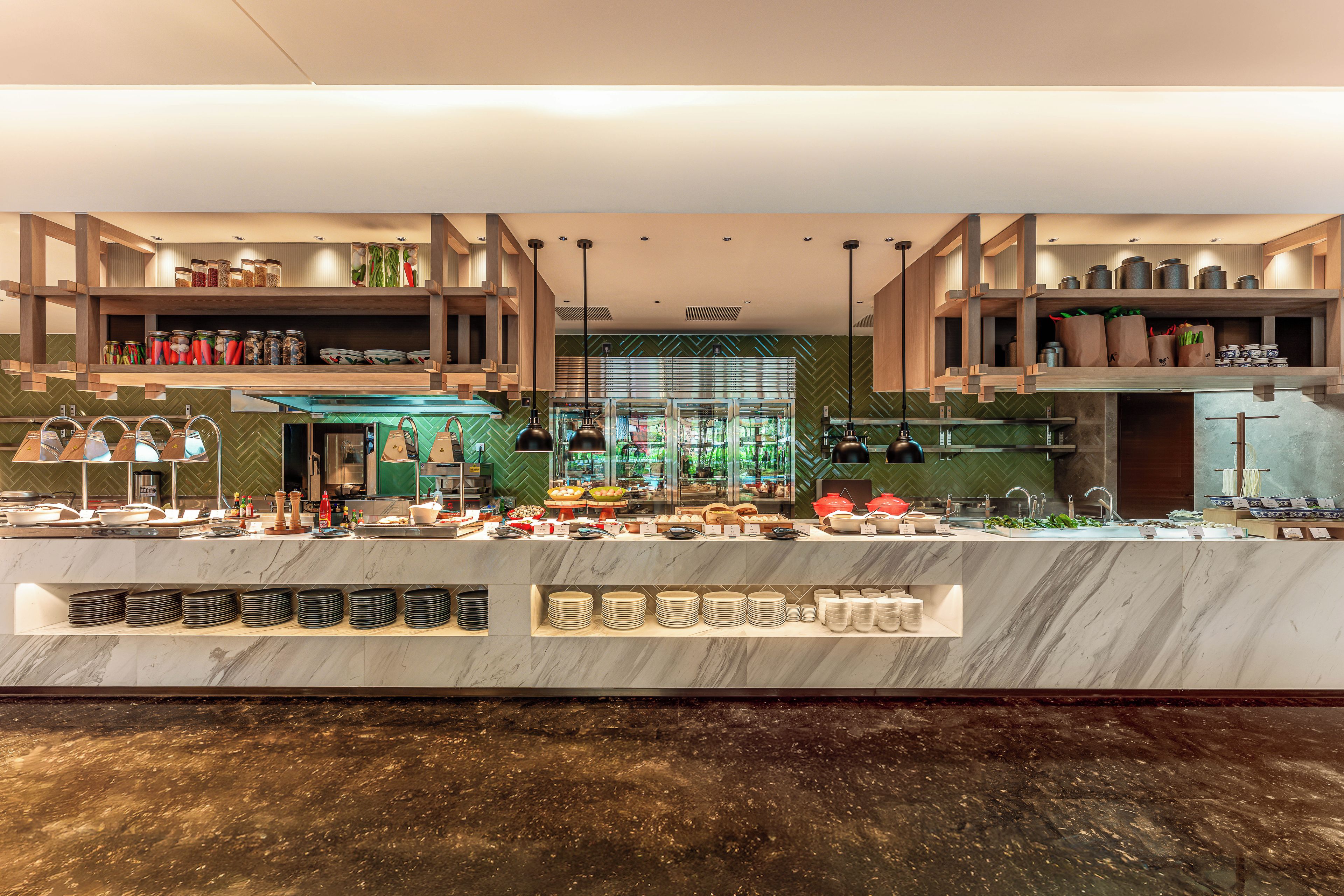 Un moderno hall de hotel con un mostrador de recepción de mármol, una zona de buffet y vistas de la ciudad a través de amplios ventanales.