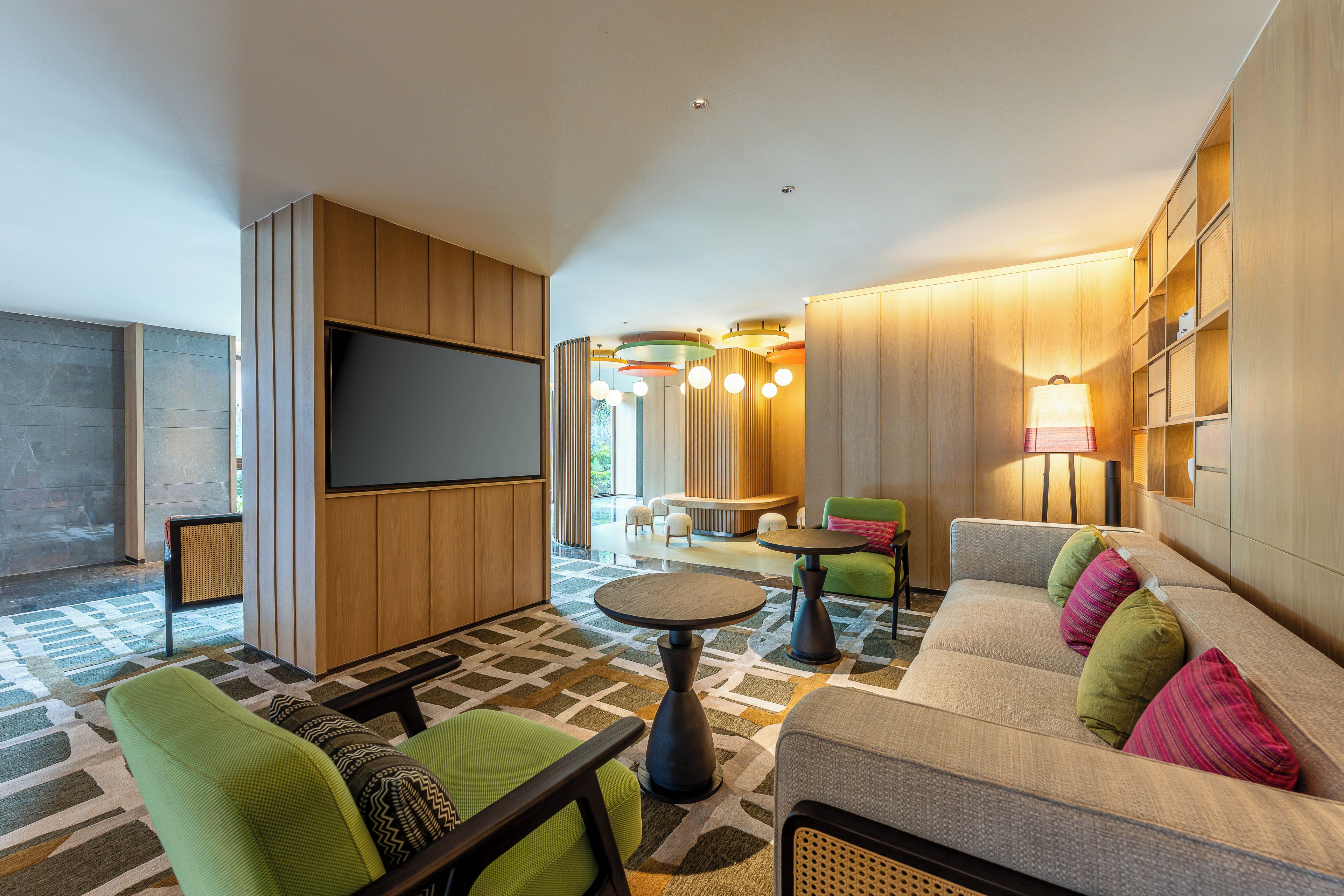Un moderno vestíbulo de hotel con televisor de pantalla plana, zona de estar con sofás y sillones, una mesa de centro y una alfombra estampada.