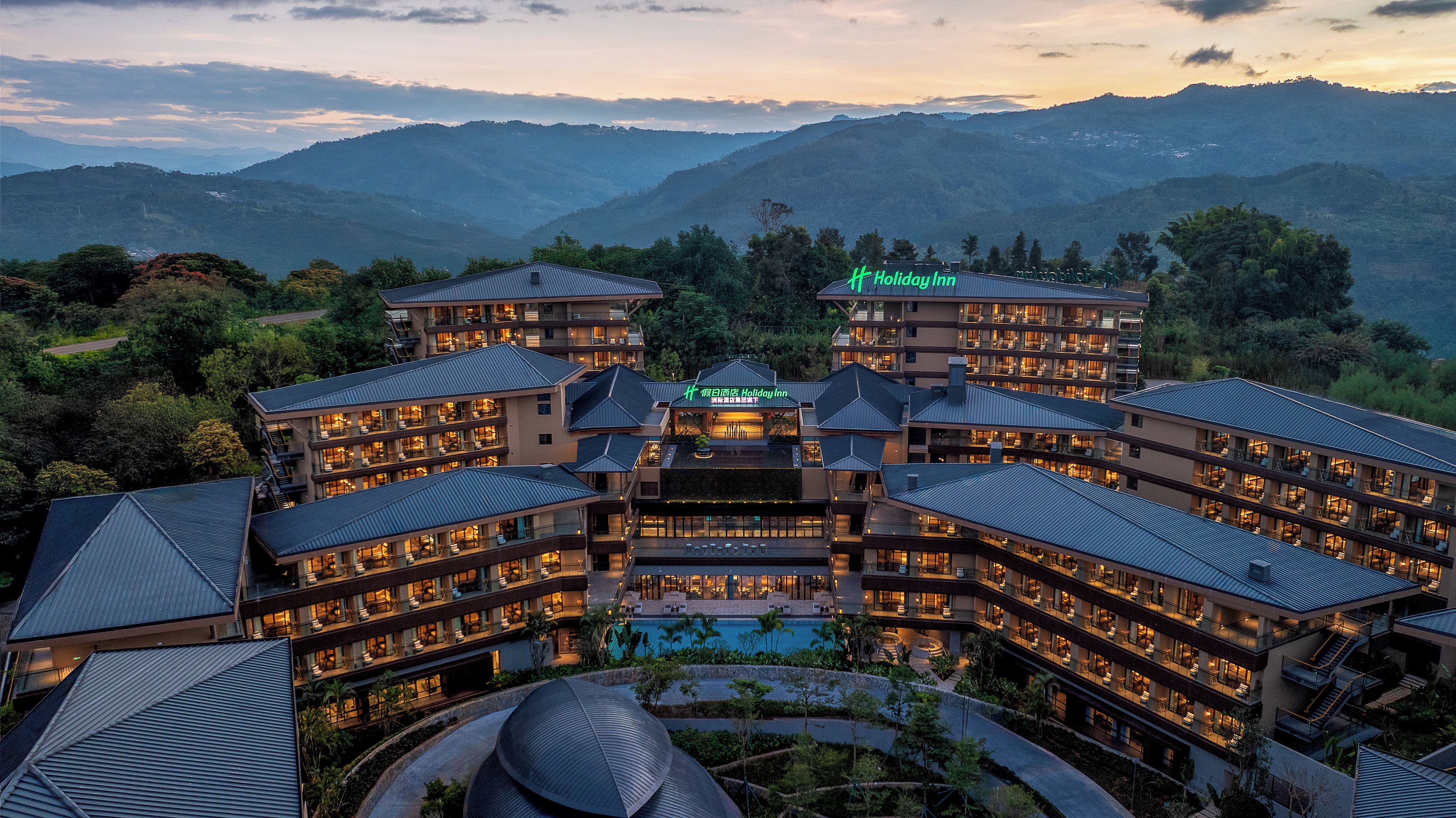 A multi-story hotel with a pool, surrounded by mountains.