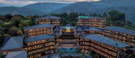 A multi-story hotel with a pool, surrounded by mountains.