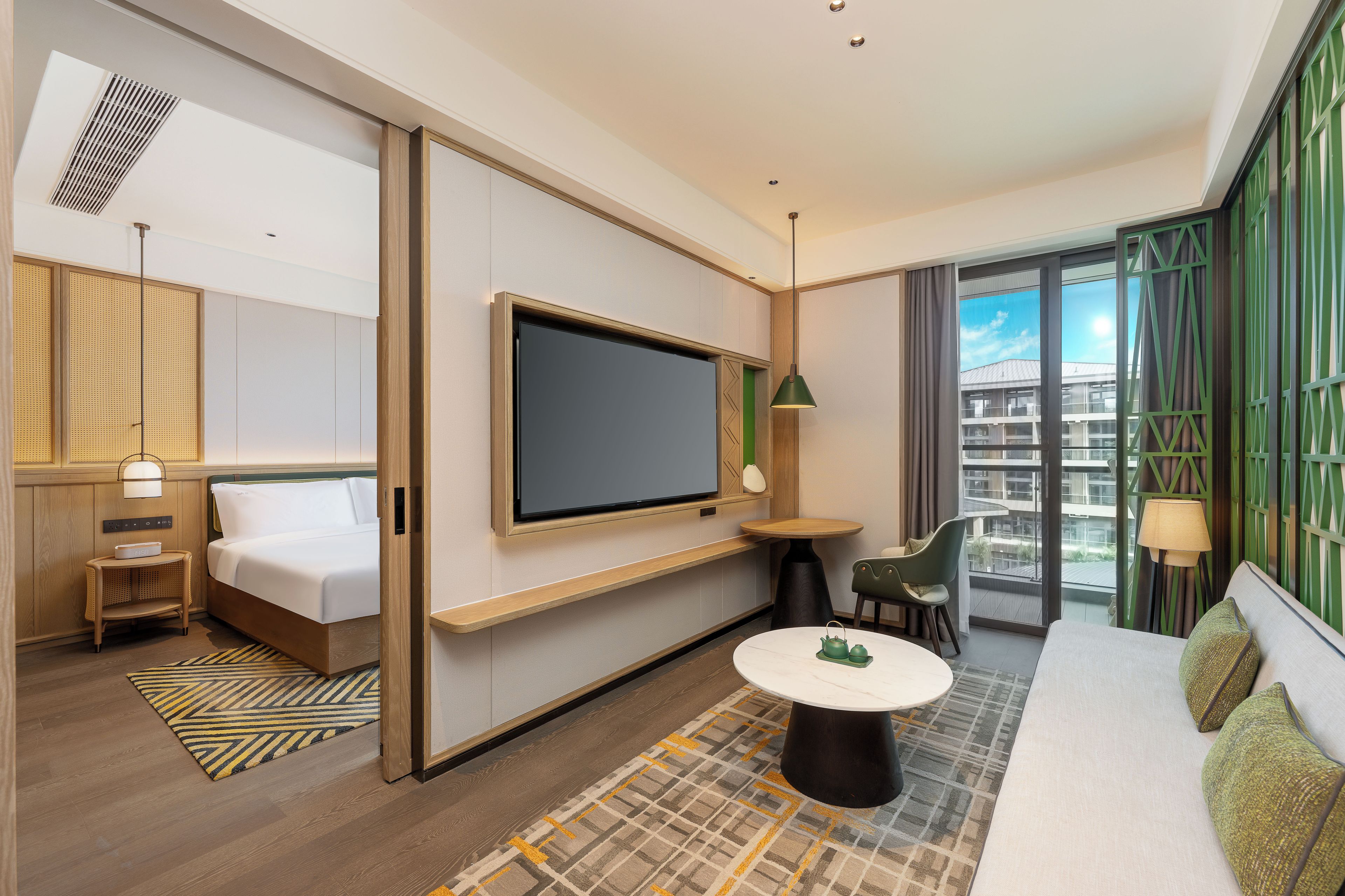 A modern hotel room with a bed, a TV, a small table, and a sofa.