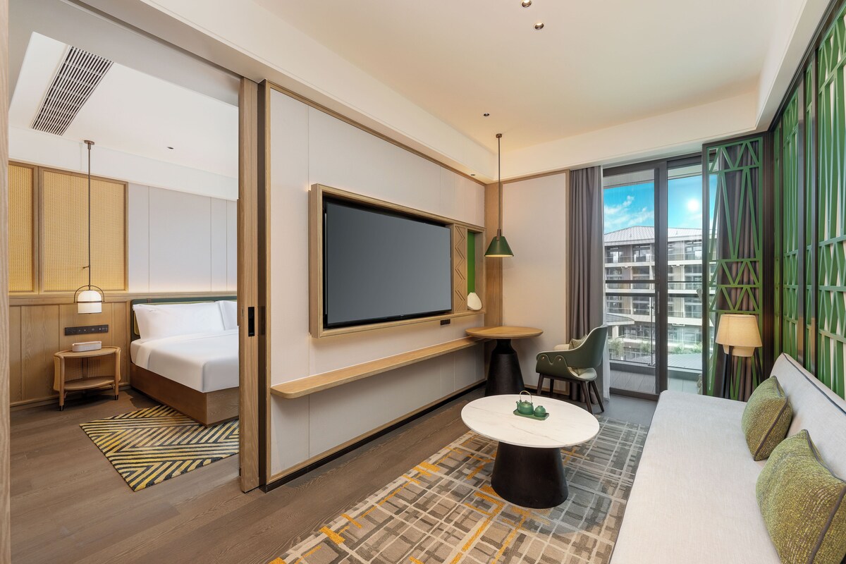 Una habitación de hotel moderna con cama, televisión, una mesita y un sofá.