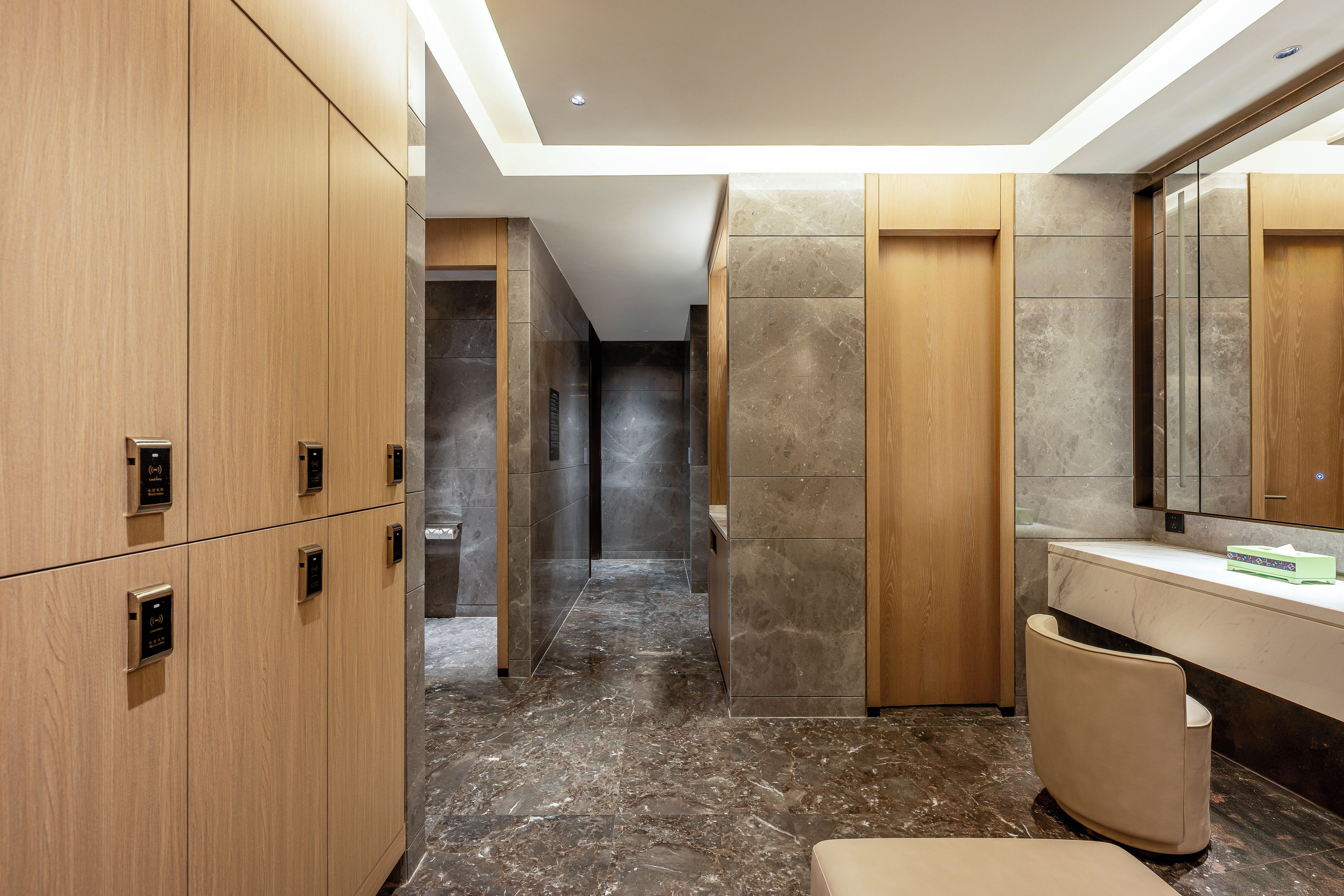Un baño moderno con piso de mármol, armarios de madera, tocador con espejo y un inodoro.
